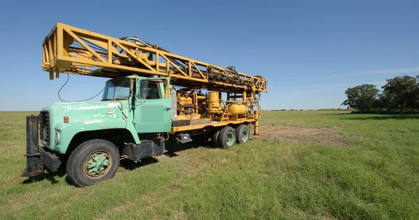 A truck-mounted borehole drilling rig parked on a grassy plot